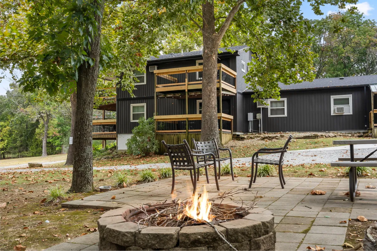 An inviting outdoor communal area featuring a fire pit surrounded by ample seating, the resort’s building facade, and the backdrop of tall trees. The warm glow and arrangement suggest evenings spent socializing, hosting group activities, or unwinding after a productive day.