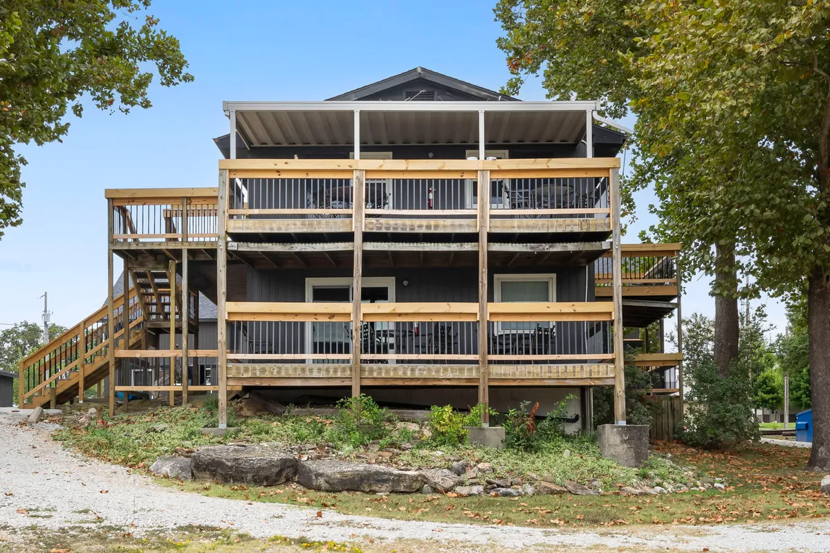A view of multiple balconies with wooden railings and a staircase, surrounded by greenery. The space suggests casual outdoor gatherings, coffee breaks, or simply soaking in the natural environment, with plenty of room for guests to spread out or mingle.