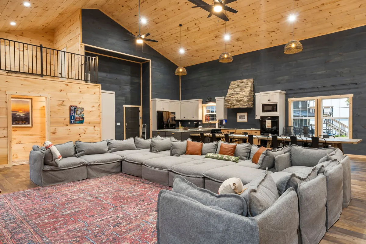 A cozy living space with a large sectional sofa, a soft rug, an adjacent kitchen area, and a charming stone fireplace. The space is arranged for family gatherings, casual dining, and relaxation—perfect for movie nights or intimate conversations.