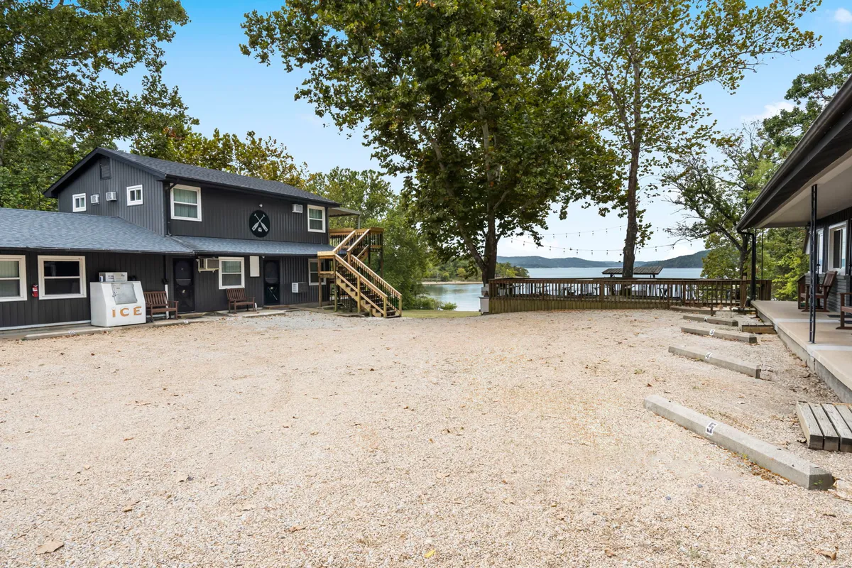 A friendly exterior shot of a two-story building with large stairs leading to a deck that overlooks the water. The surrounding trees and ample deck area suggest a perfect space for group gatherings, outdoor dining, and enjoying sunset views.