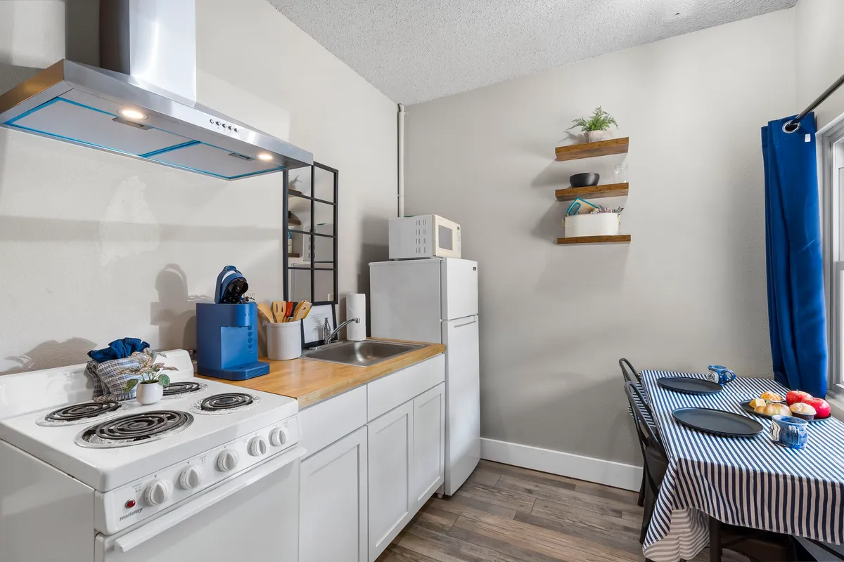 A cozy kitchen and dining space featuring a kitchen stove, sink, a dining table ready for group meals, and shelves decorated with plants. Guests are seen sharing meals and stories, echoing the communal spirit of the resort.