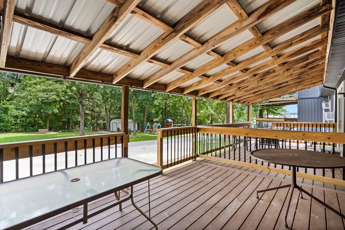 A spacious wooden deck with overhead cover, outdoor furniture, and a green landscape beyond. The area is ideally suited for group gatherings, outdoor dining, and relaxation, capturing a welcoming and communal vibe.