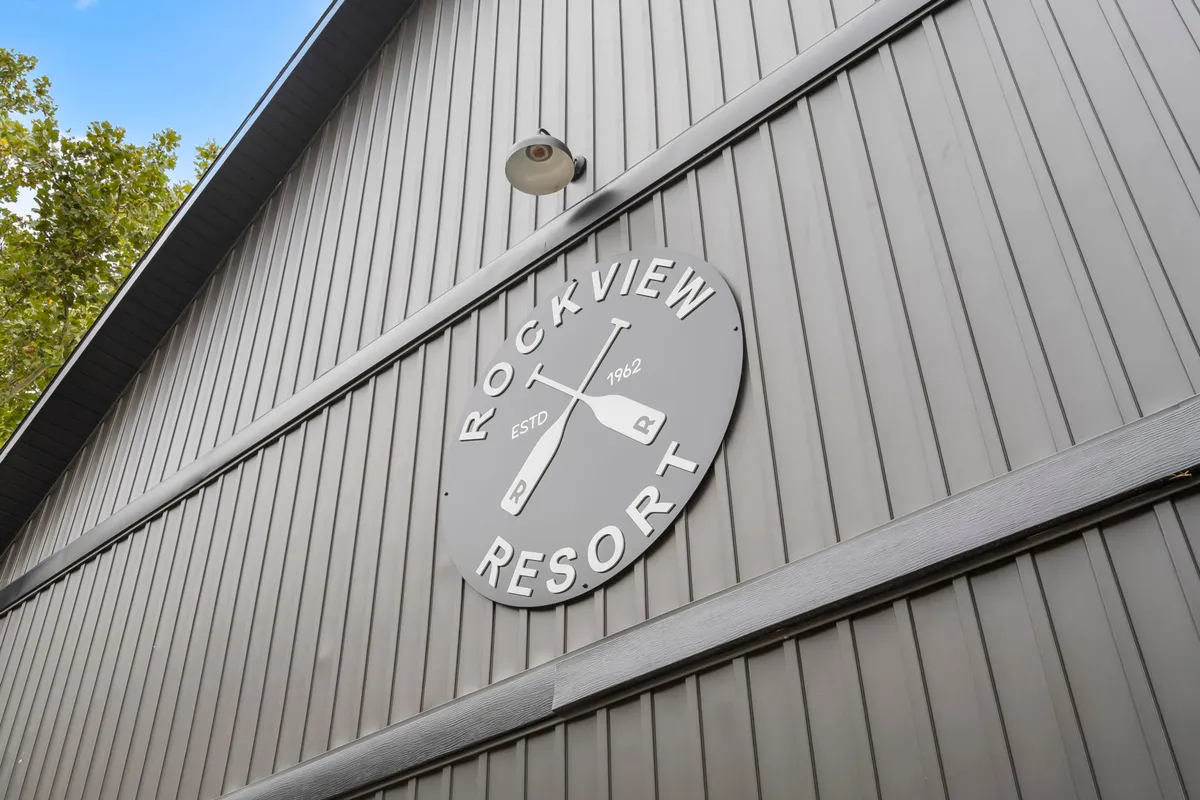 A welcoming view of the Rock View Resort entrance, featuring the resort sign, wooden building exterior, and surrounding trees. The scene suggests arrival, excitement, and the beginning of a family adventure in a natural setting.